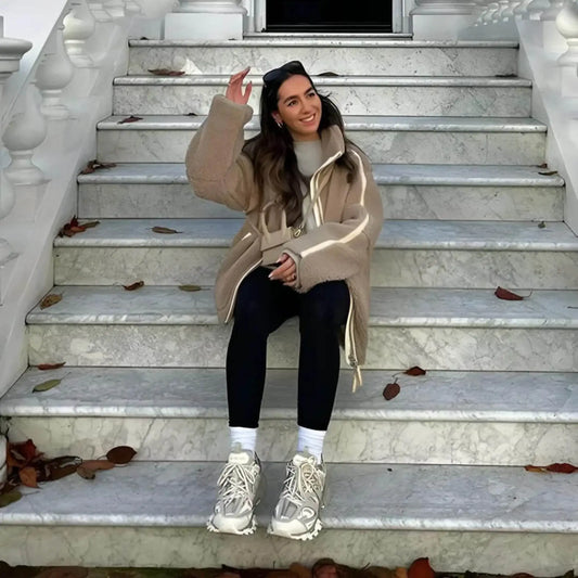 Woman in beige shearling jacket, black leggings, and chunky sneakers sitting on marble stairs outdoors