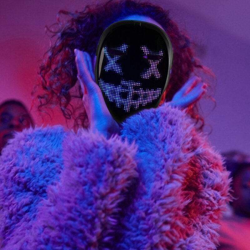 Person wearing LED light up mask with pixelated face design and fluffy jacket in neon lighting