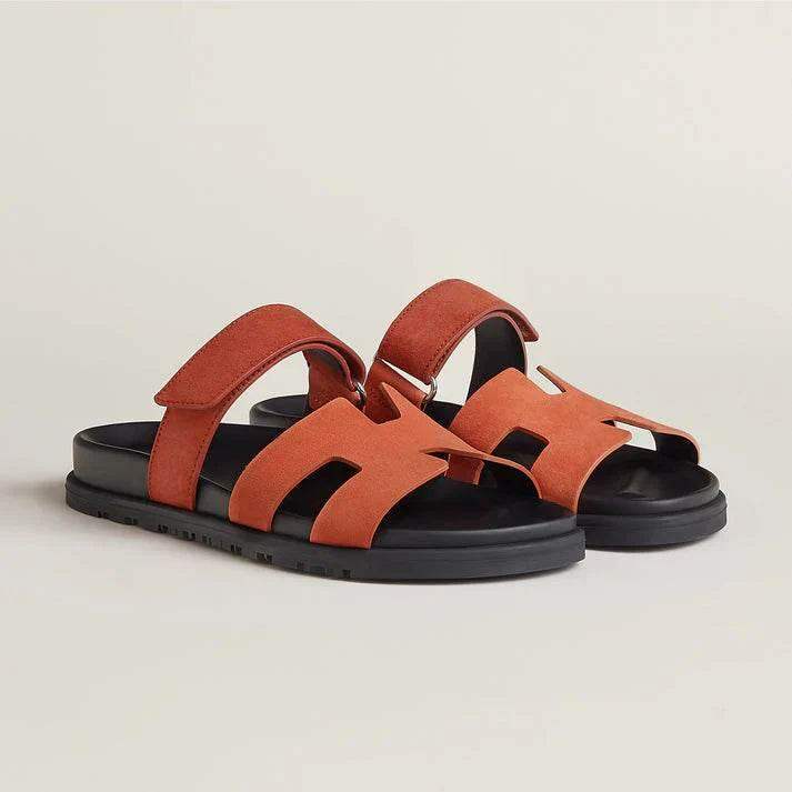 Orange suede open-toe sandals with black soles and adjustable straps on a neutral background