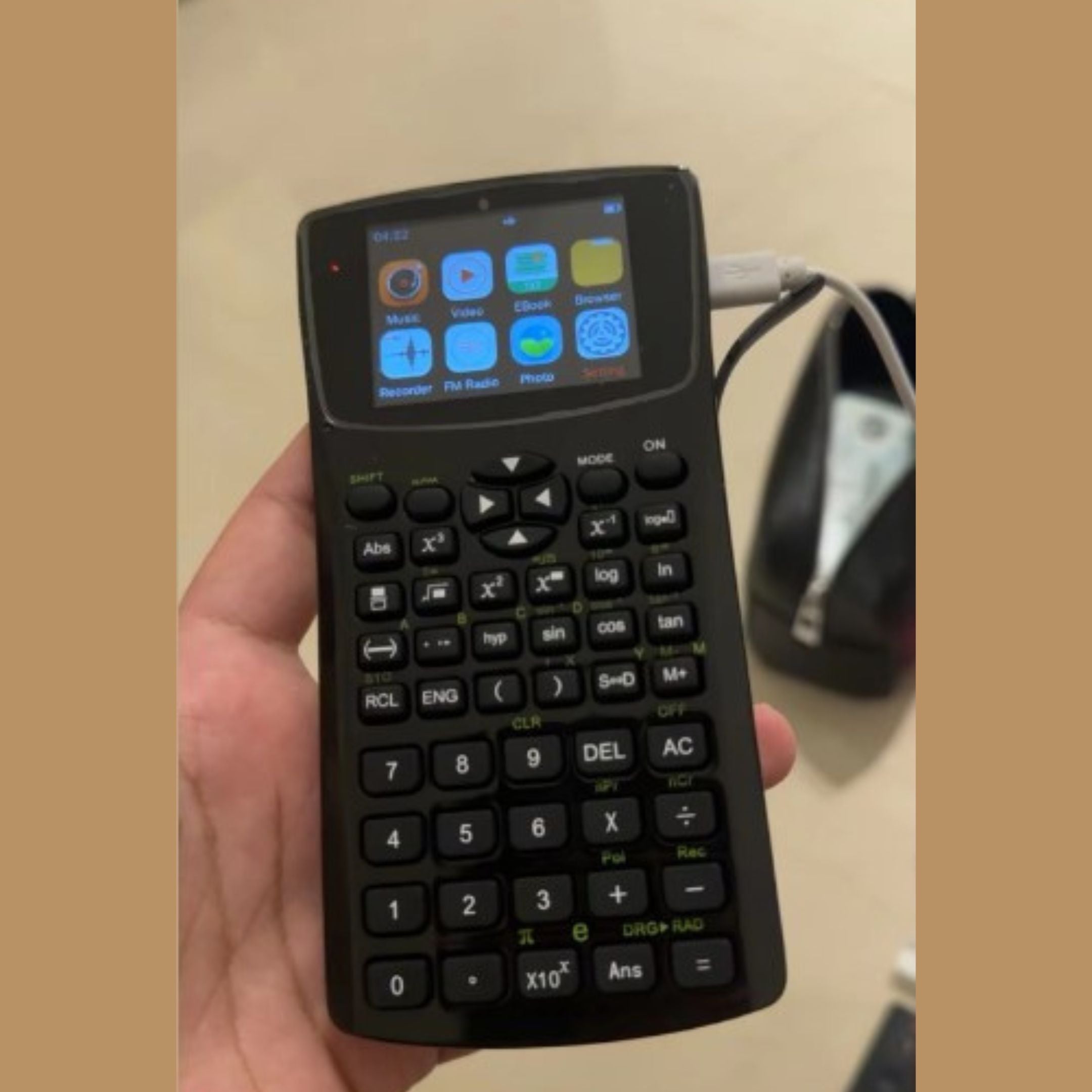 A person holds a small, black handheld gaming device connected to a large screen displaying a pixelated video game with bricks, sky, and a green hill. The game has text showing WORLD 1-1 and various numbers.