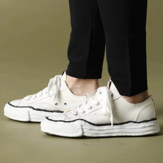 White fashion sneakers with thick soles and black trim, worn with black pants on a beige floor.
