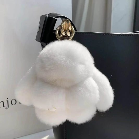 Soft white plush paw keychain bag charm with gold clasp hanging on a black handbag