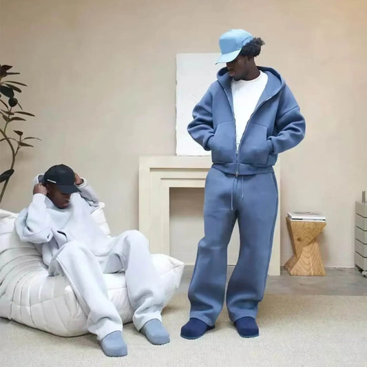 Two men wearing relaxed fit loungewear sets and caps in a modern living room setting.