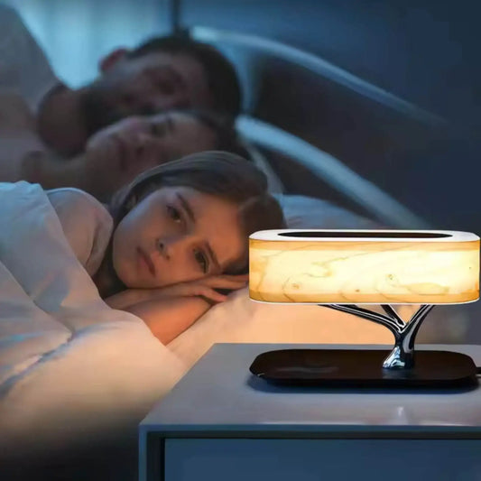 Modern tree-shaped bedside lamp glowing on nightstand beside child and adults in bed