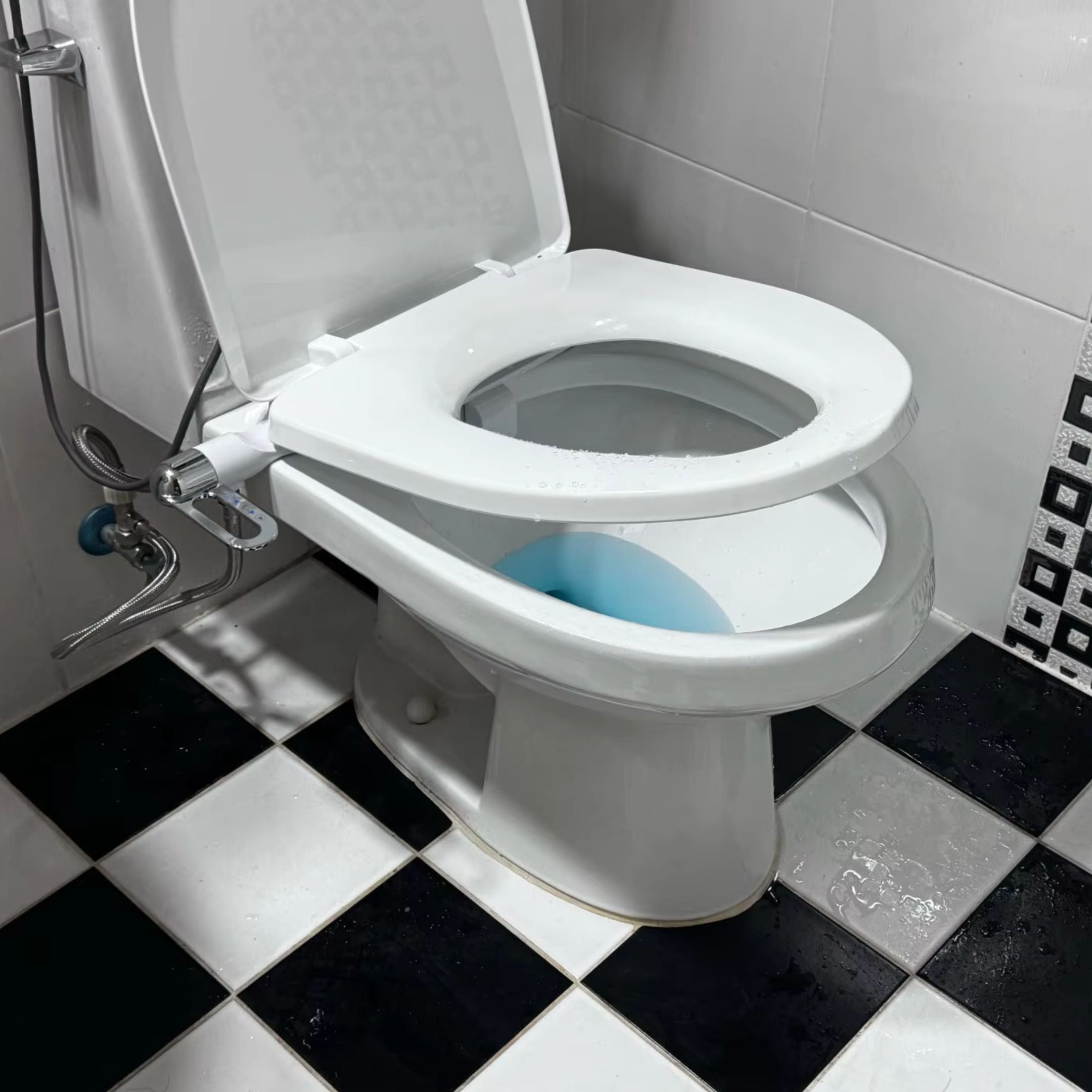 Open toilet seat in a bathroom with black and white tiled floor.
