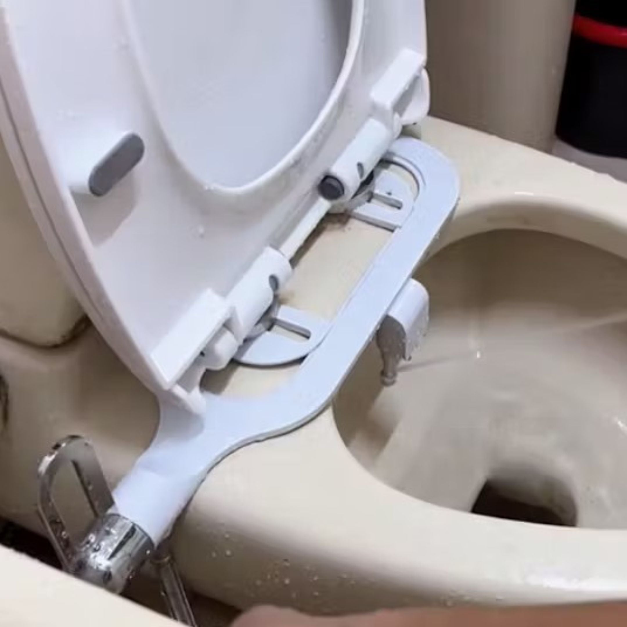 A bidet shower head aimed into an open toilet bowl with seat and lid up.